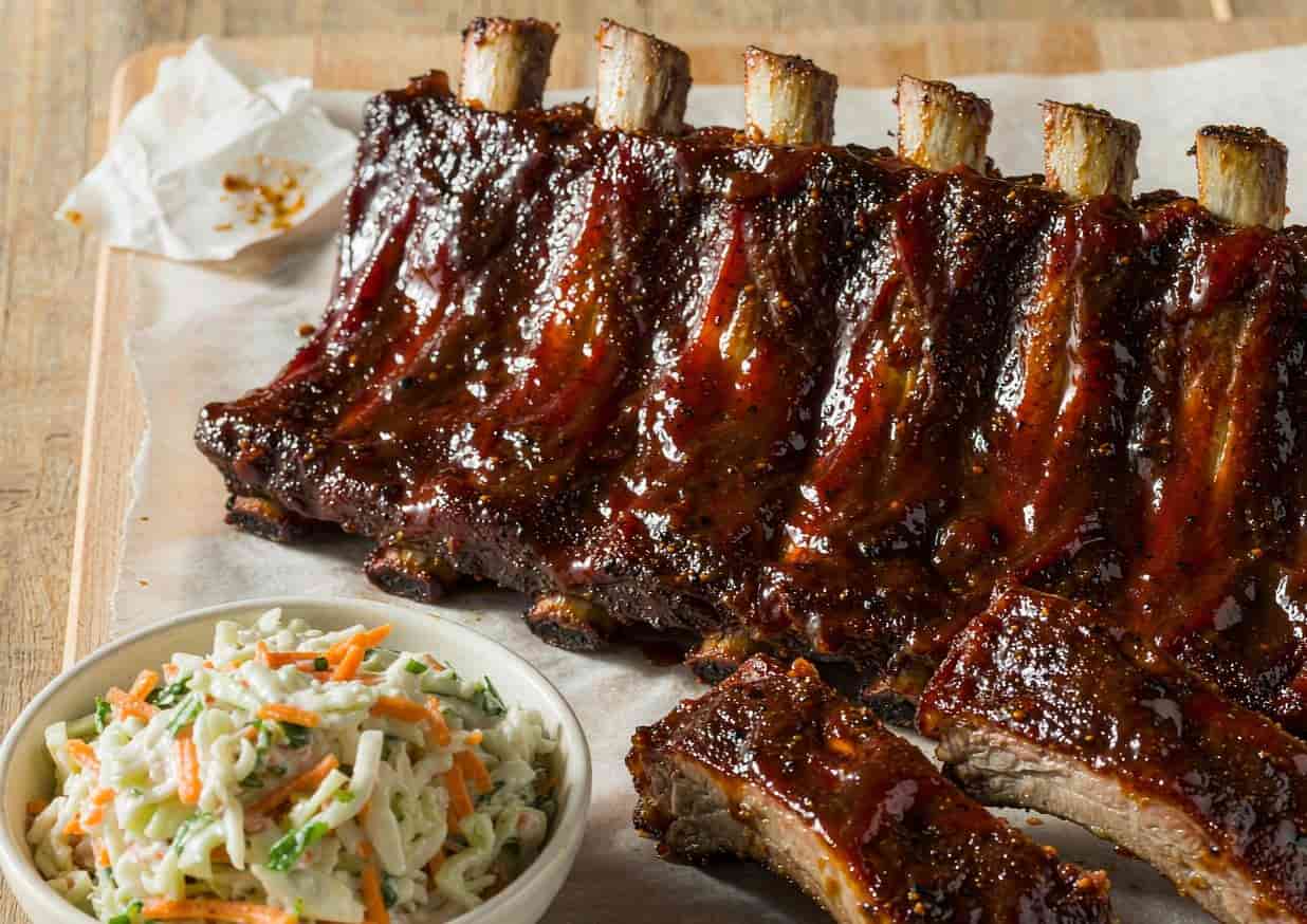 A rack of glazed BBQ baby back ribs with a side of coleslaw
