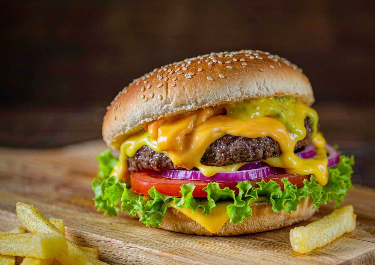 A classic American cheeseburger with melted cheese, lettuce, tomato, and onion on a wooden board
