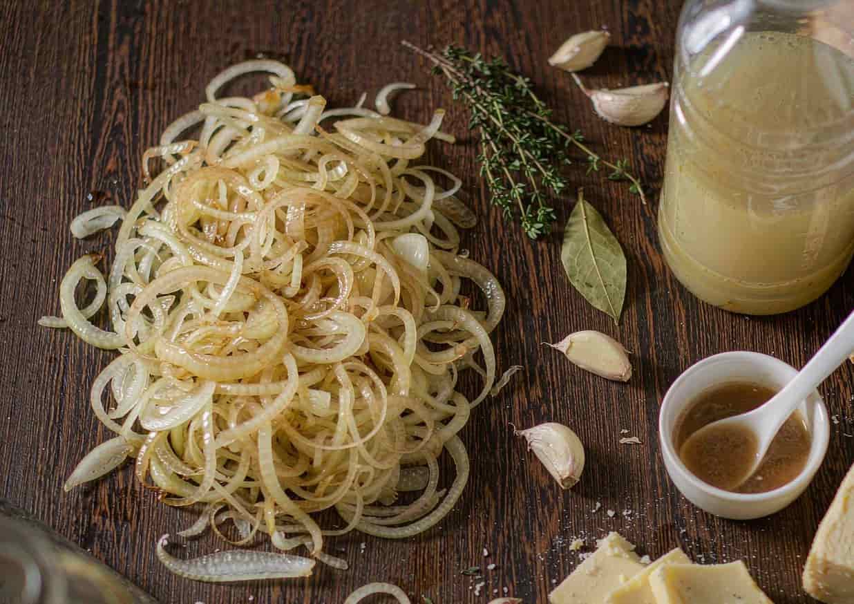Overhead flat lay of French onion soup ingredients including sliced onions, baguette, and Gruyere