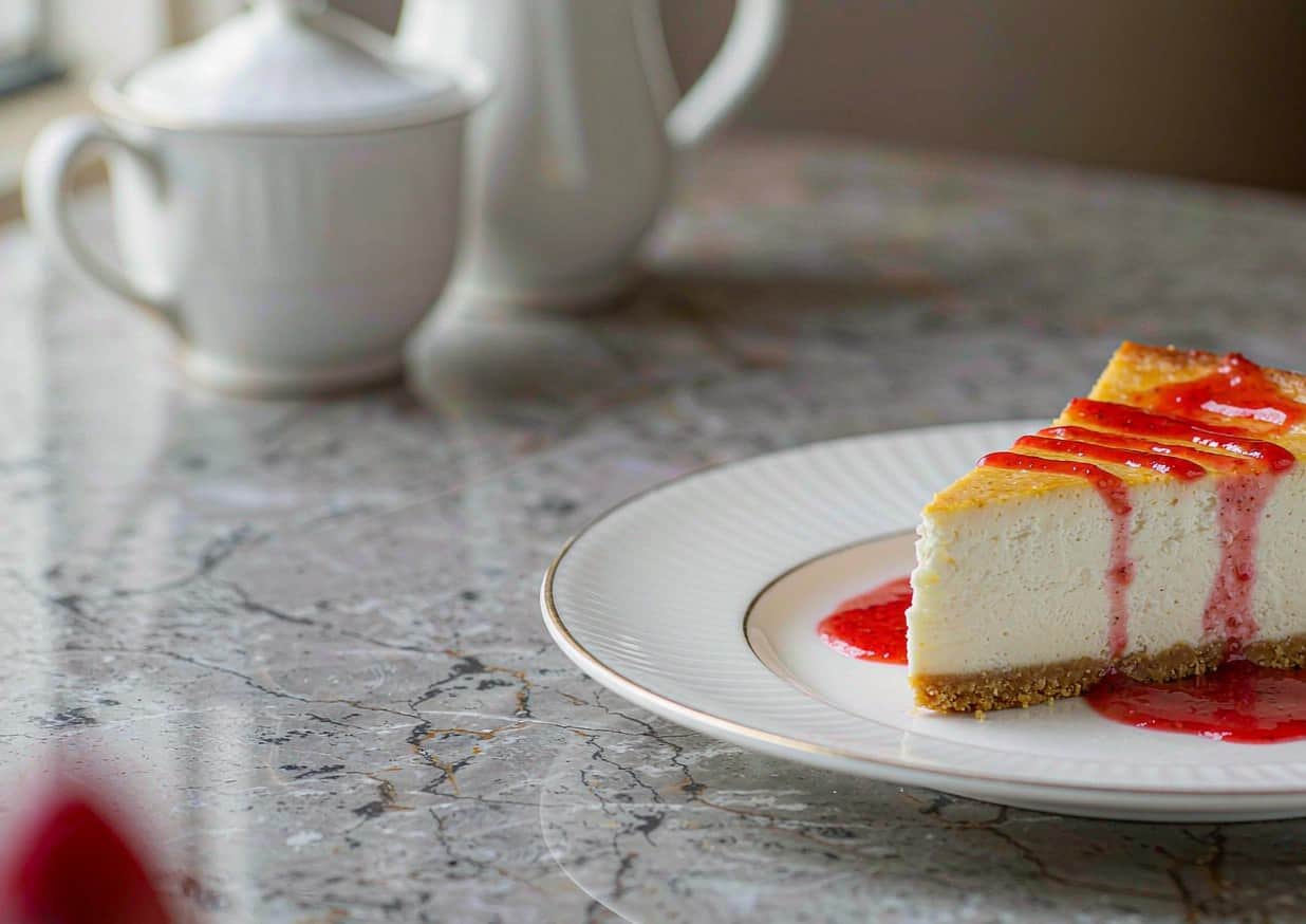 A slice of New York-style cheesecake on a white plate with strawberry coulis