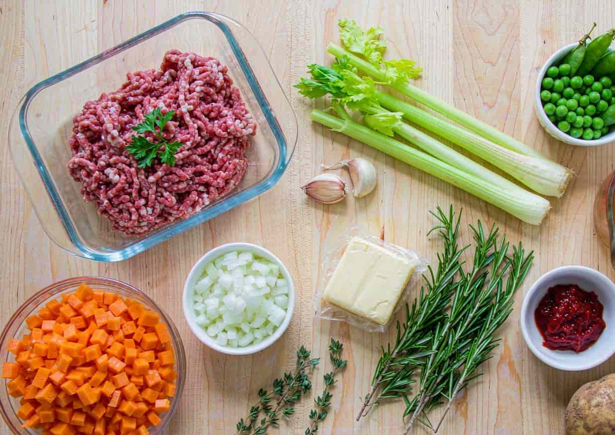 Overhead flat lay of shepherd's pie ingredients including ground lamb, carrots, potatoes, and peas