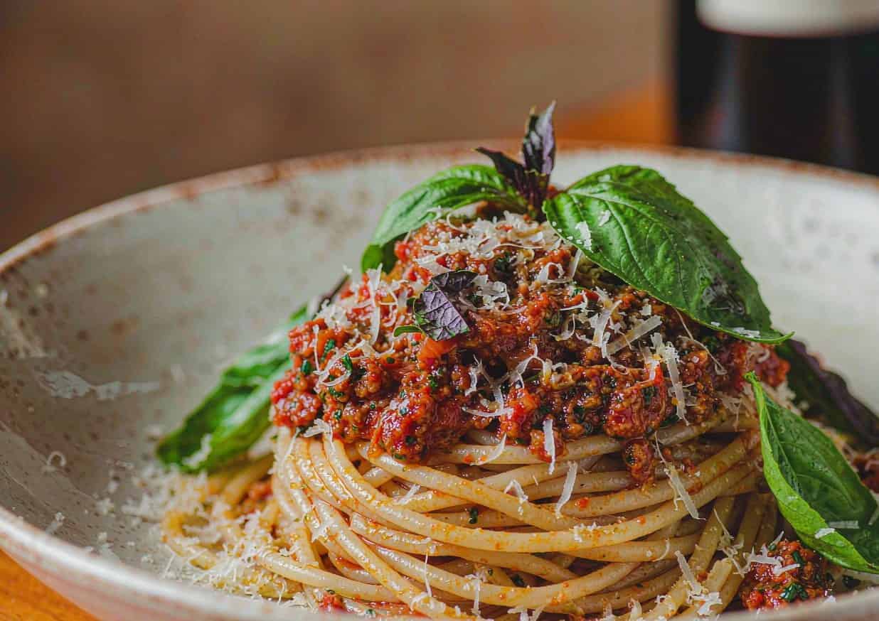 Bowl of spaghetti Bolognese topped with grated Parmigiano-Reggiano and torn basil