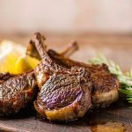 Grilled lamb chops resting on a board with char marks, rosemary sprigs and lemon wedges