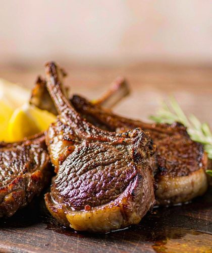 Grilled lamb chops resting on a board with char marks, rosemary sprigs and lemon wedges