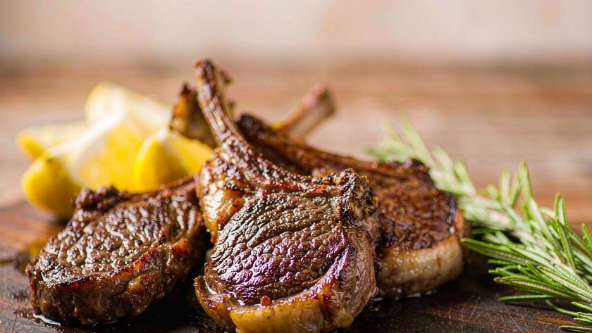 Grilled lamb chops resting on a board with char marks, rosemary sprigs and lemon wedges