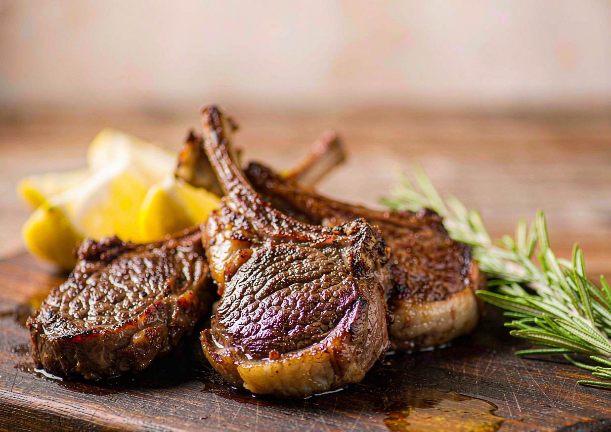 Grilled lamb chops resting on a board with char marks, rosemary sprigs and lemon wedges