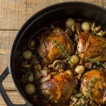 Coq au vin in a cast-iron casserole with browned chicken pieces, mushrooms and pearl onions in a glossy red wine sauce