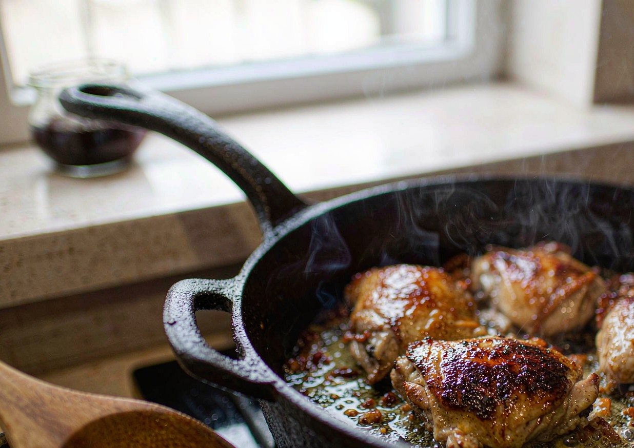 Chicken pieces browning skin side down in a cast-iron casserole with rendered lardons