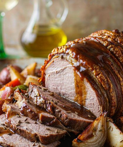 Sliced German pork roast with a crackled brown crust on a platter with pan gravy, roasted root vegetables, and caraway seeds