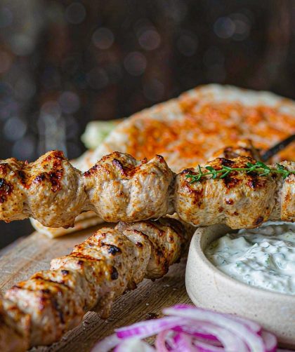Grilled chicken souvlaki skewers on a platter with tzatziki, sliced red onion, and warm flatbread