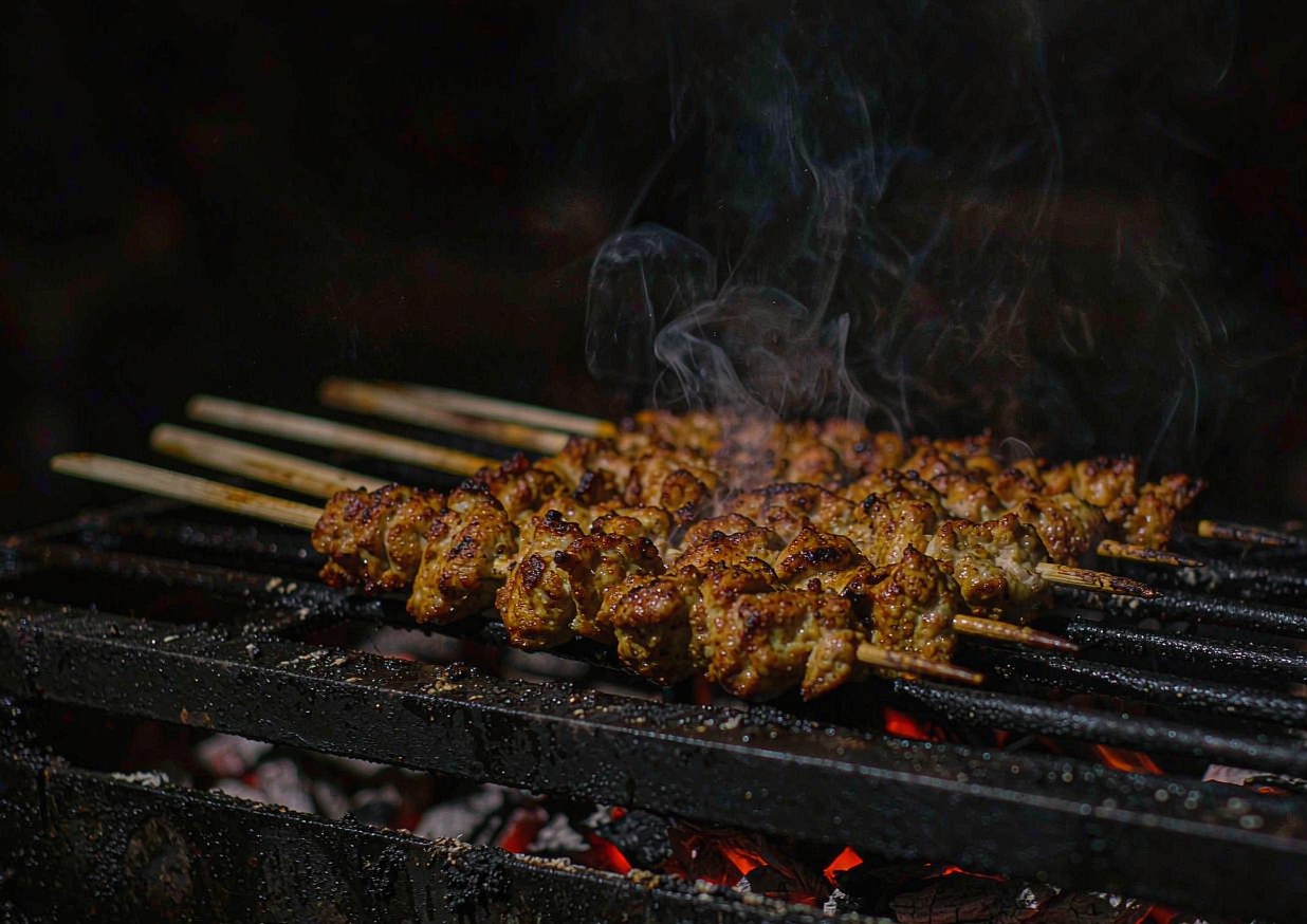 Chicken skewers cooking on a grill grate over glowing coals with light char marks
