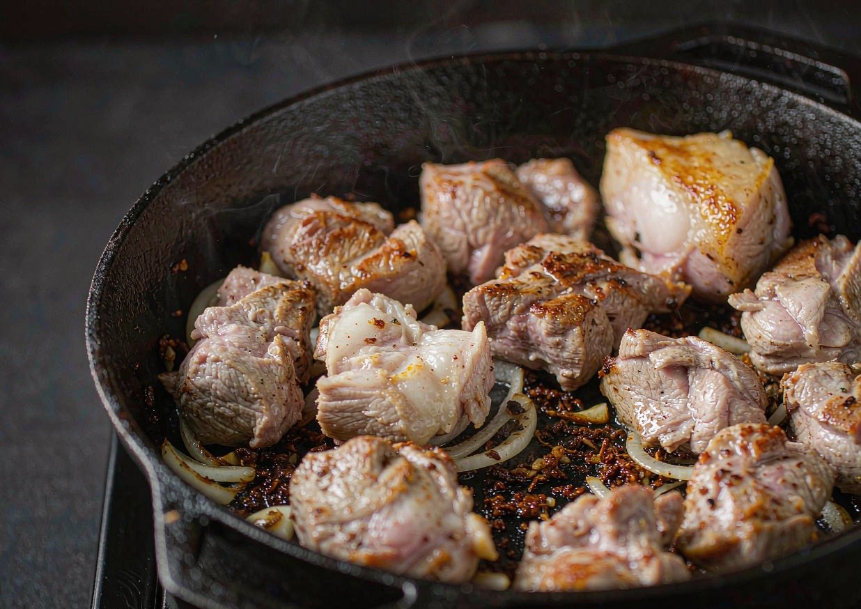 Pieces of pork shoulder browning in a cast-iron Dutch oven before the braising liquid goes in