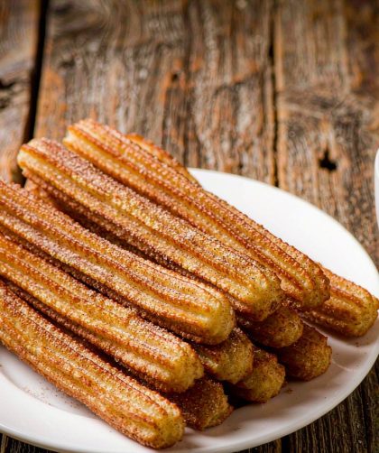 Golden ridged Spanish churros piled on a plate with cinnamon sugar beside a cup of thick hot chocolate for dipping