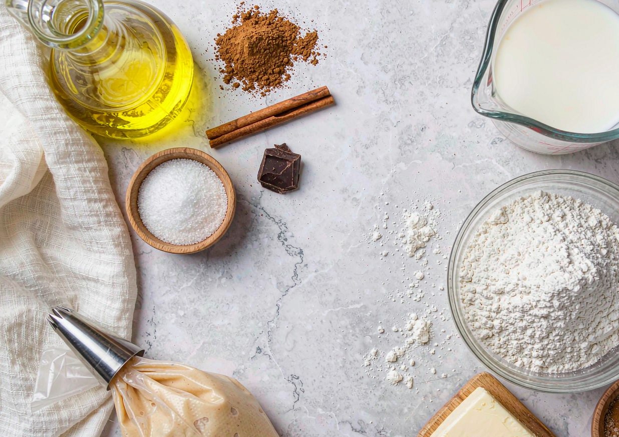 Overhead flat lay of churros ingredients including flour, eggs, butter, oil for frying, sugar, cinnamon and dark chocolate