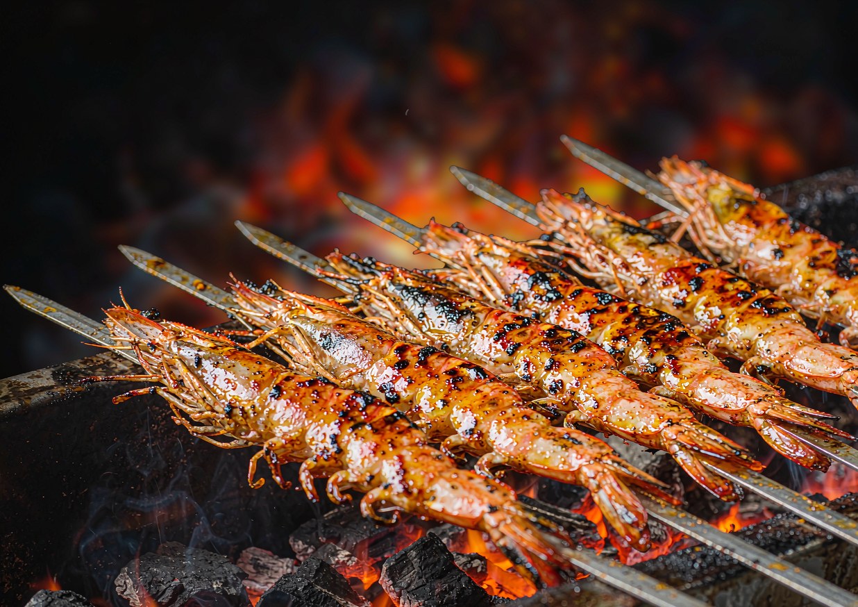 Skewered shrimp grilling directly over a grate above glowing coals with smoke rising