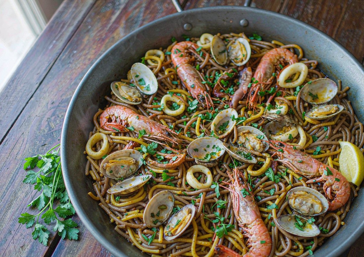 Spanish seafood fideua in a wide paella pan with prawns, clams and toasted noodles