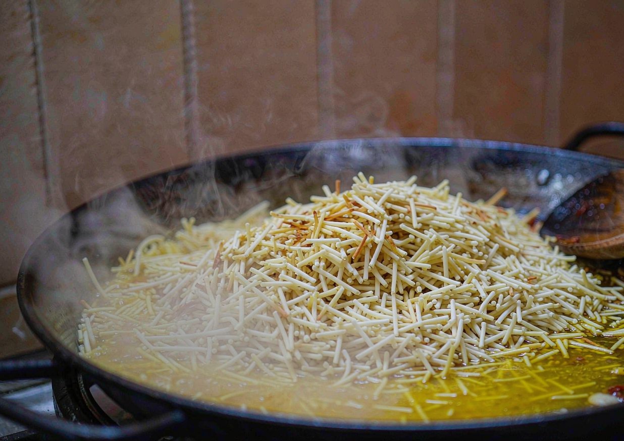 Fideus noodles toasting in a wide paella pan with garlic and olive oil before the stock is added